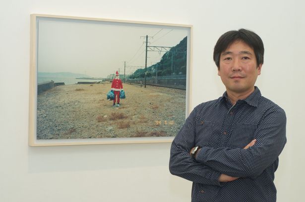 Japanese artist Shimabuku next to a summer picture of himself dressed up as Santa