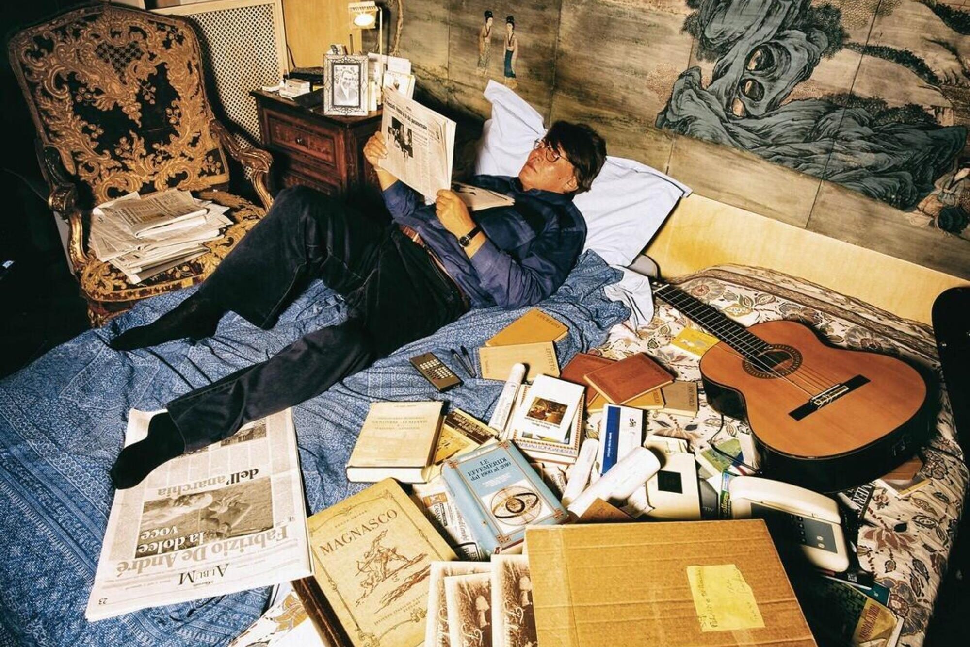 50 anni di Guido Harari: Fabrizio de Andrè ritratto sul suo letto nella casa a Milano mentre sfoglia delle riviste